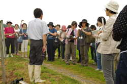 無農薬実験米の田んぼで生産者の説明を熱心に聞く参加者